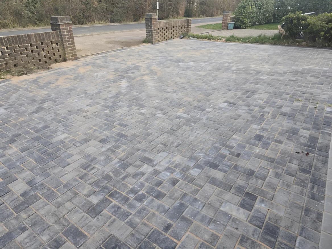 A finished charcoal block paving driveway with a contrasting soldier-course border, framed by a low brick wall.